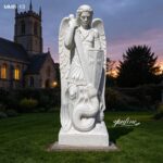 St Michael the Archangel marble statue with detailed wings, set against a church backdrop at dusk