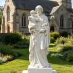 Hand-carved white marble St Joseph statue holding baby Jesus, placed in a church garden, crafted by YouFine.