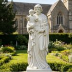 Hand-carved life-size marble St Joseph statue cradling baby Jesus, set in a lush church garden with blooming flowers.