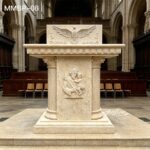 Carved beige marble pulpit with Holy Spirit dove on top and saint figure, stone lectern for church interior