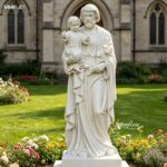Life-size marble St Joseph statue holding the Holy Infant, placed in a private home garden with flowers and greenery.