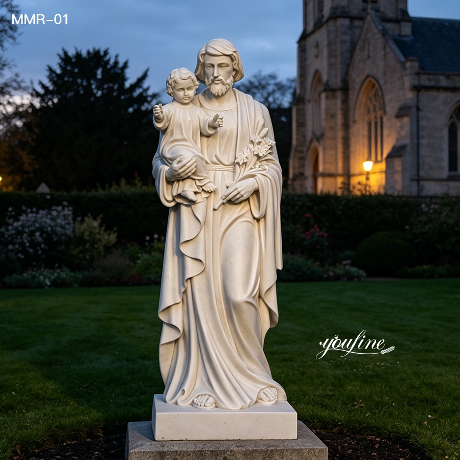 Hand-carved marble St Joseph statue with baby Jesus, lit at night in a peaceful church garden setting.