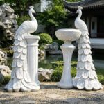 Outdoor white marble peacock planter statue beside a garden pond and rocks