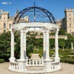 Elegant white marble gazebo with twisted columns and black wrought iron dome, placed in a historic castle garden setting
