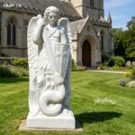 Hand-carved marble St Michael the Archangel statue with sword and shield, standing on a snake in a churchyard
