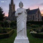 A serene marble St. Jude statue illuminated by sunset light, placed in a quiet church courtyard.