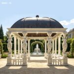The caryatid column marble gazebo positioned near a garden fountain, showcasing its elegant design.