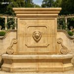 Handmade beige marble wall fountain in a structured garden with stone balustrades