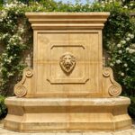 Hand-carved stone wall fountain with scroll details in front of climbing roses