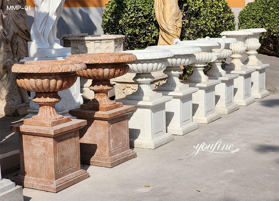 Row of marble planters in red, white, and beige tones, with carved pedestals, factory display.