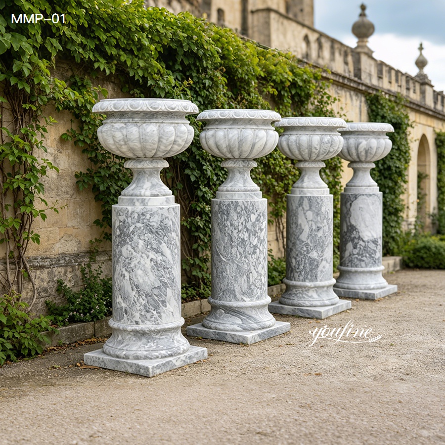 Set of grey marble planters with smooth pedestals, arranged in a row in a garden.