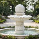 White rolling marble ball fountain placed in an elegant courtyard, featuring hand-carved pedestal relief and smooth water flow.