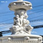 Upper basin and seated figure detail of a large marble lion water fountain outdoor.