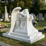 Life size white marble weeping angel memorial statue against green tree cemetery scenery