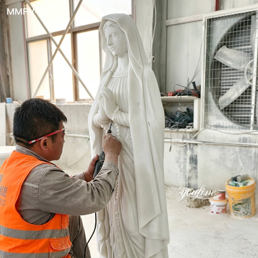 Skilled artisan polishing natural white Our Lady Of Lourdes marble statue, handmade carving process in stone sculpture workshop