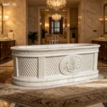 Hand carved marble bathtub placed under crystal chandelier inside grand vintage styled marble bathroom