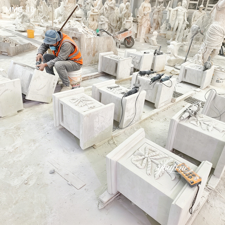 Artisan in safety gear carving intricate marble blocks in a workshop surrounded by sculptures and tools.