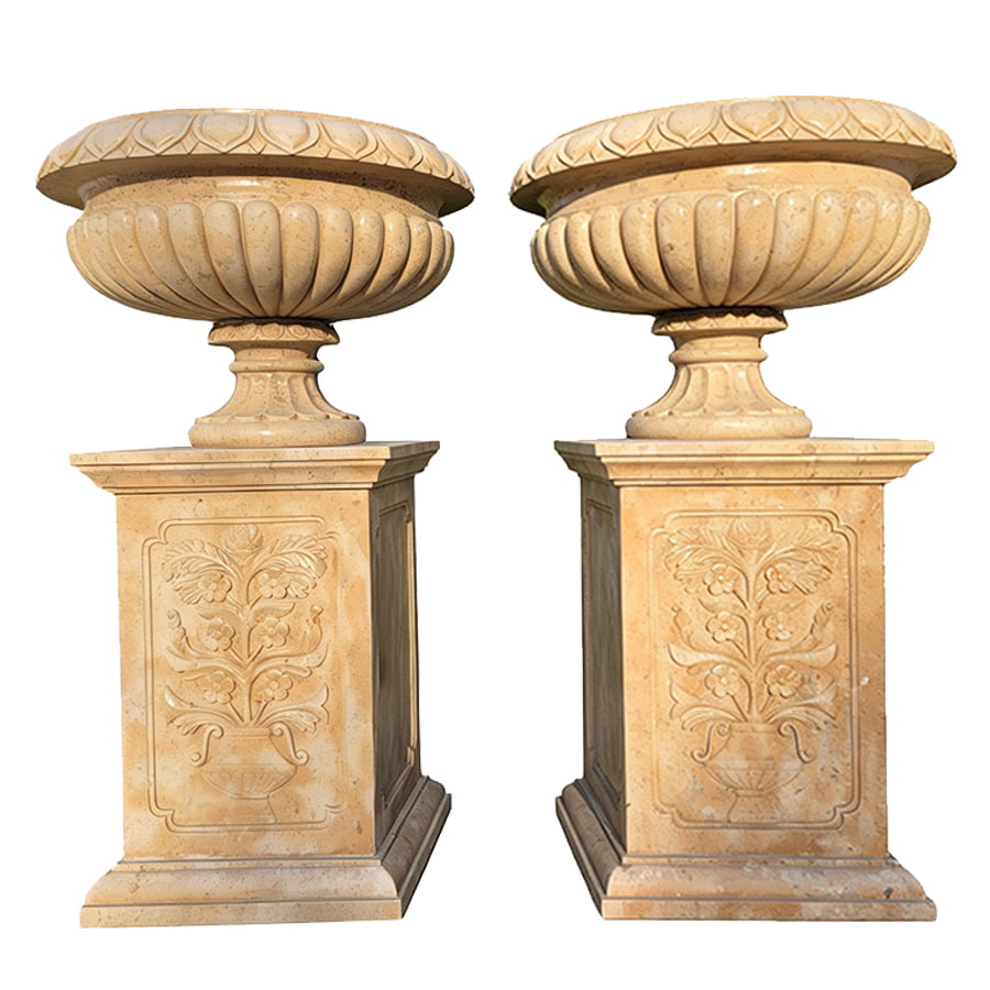A pair of intricately carved marble urns resting on ornate pedestals, each adorned with floral motifs, against a white background.