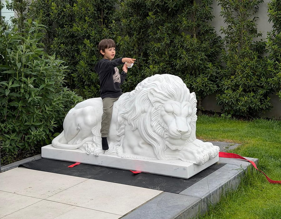 Child posing on a marble lion sculpture outdoors