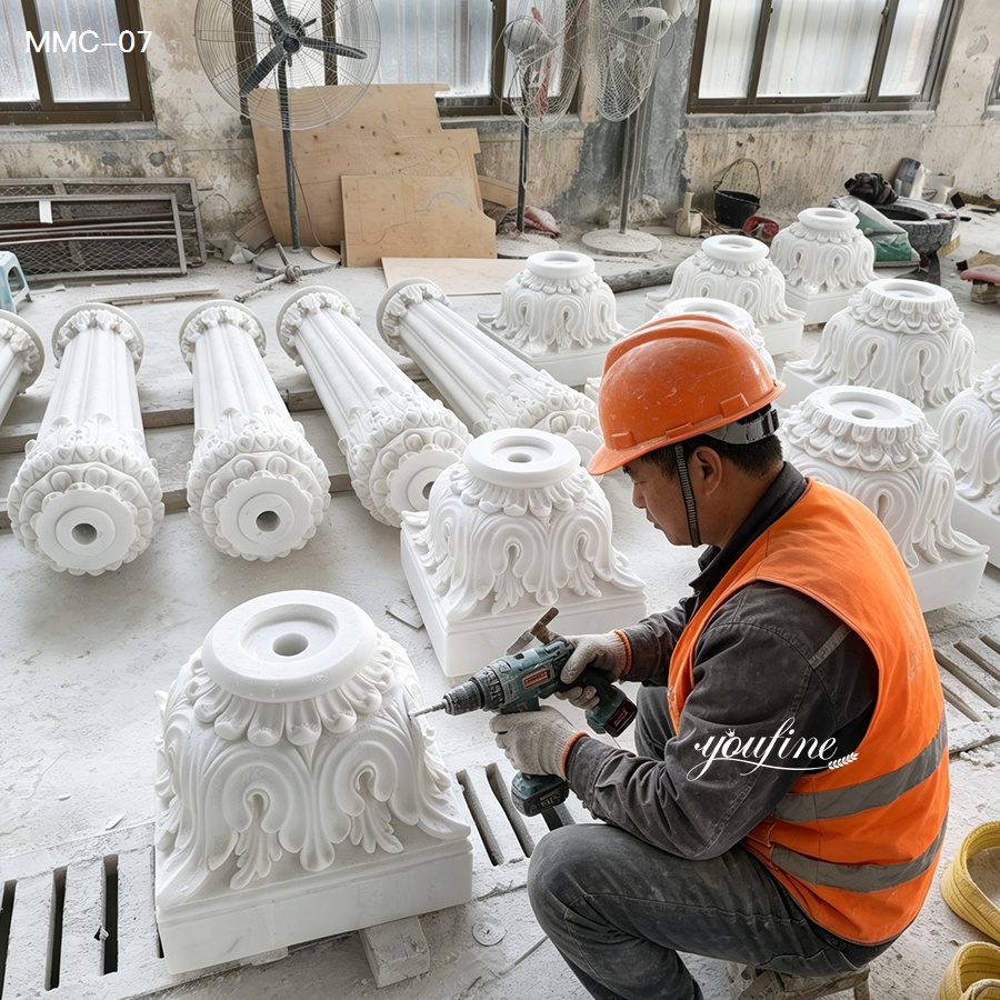 A craftsman in an orange safety vest and helmet working on intricately carved marble column bases with a drill in a workshop.