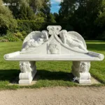 Intricately carved marble bench featuring reclining angels and floral motifs, placed in a lush garden under clear skies.