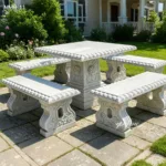 An elegant outdoor marble dining set featuring a rectangular table with intricate floral carvings and four matching benches in a lush garden setting.