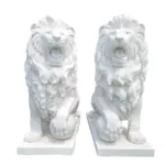 A pair of intricately carved white marble lion statues with detailed manes and fierce expressions, positioned on solid bases.