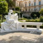 White marble sculpture depicting a woman reading, set in a formal garden with historic architecture and lush greenery.