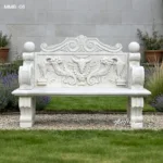 Elegant marble bench with detailed carvings featuring floral designs, animals, and scrollwork, placed in a manicured garden setting.