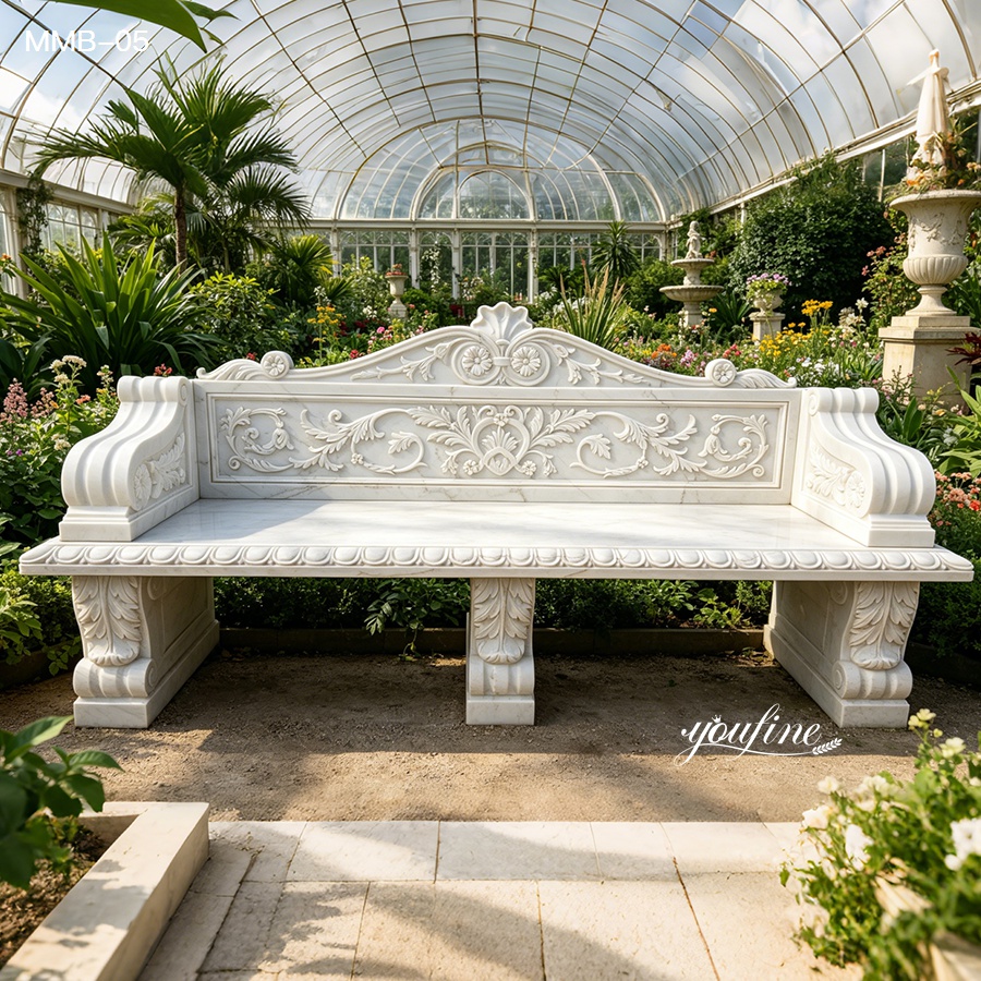 Intricately carved white marble bench with floral details placed within an elegant greenhouse surrounded by lush greenery and blooms.