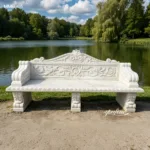 Elegant white marble bench with intricate carvings placed on a lakeside in a green park, surrounded by trees and tranquil scenery.