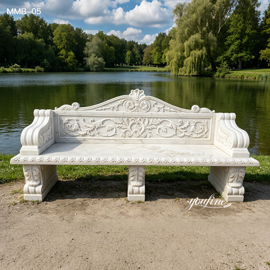 Elegant white marble bench with intricate carvings placed on a lakeside in a green park, surrounded by trees and tranquil scenery.