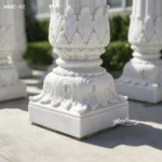 Elegant white marble column base featuring intricate leaf and scroll carvings, placed outdoors with natural lighting.