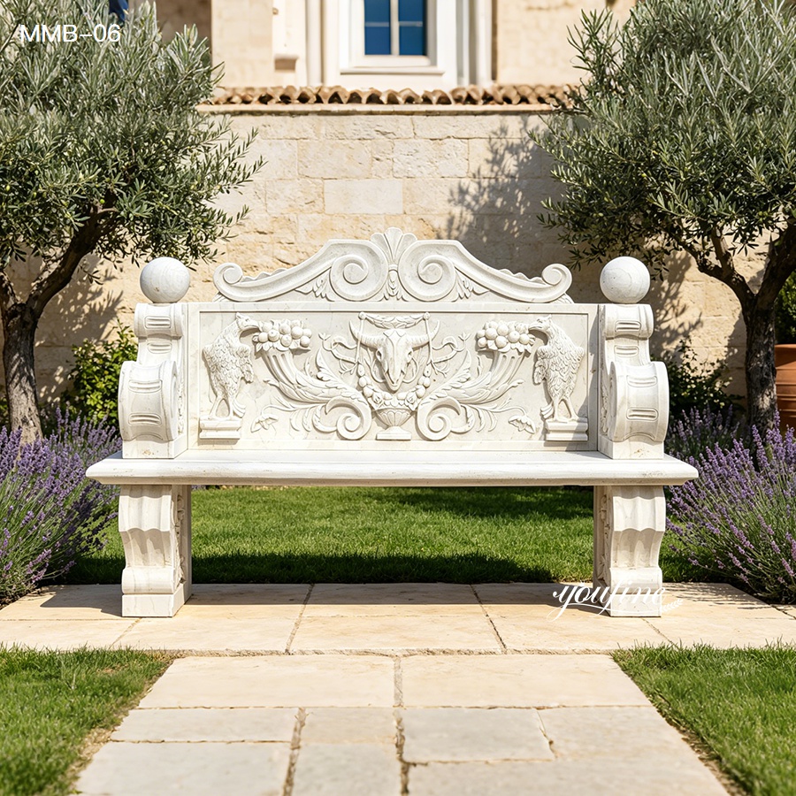 Elegant carved marble bench featuring intricate floral and bird motifs set in a vibrant garden with lavender and olive trees.