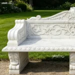Elegant marble garden bench featuring intricate floral carvings and detailed design, set in a lush garden setting.