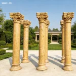 Six ornate marble columns with intricate capitals standing on a paved surface in a meticulously landscaped garden.