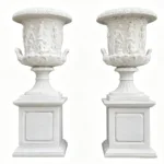 Pair of white marble planters with intricate classical figure carvings on pedestals, showcasing decorative artistry.