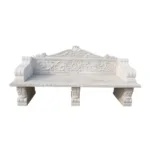 An elegant white marble bench featuring intricate floral and scrollwork carvings on the backrest and armrests, supported by carved legs.