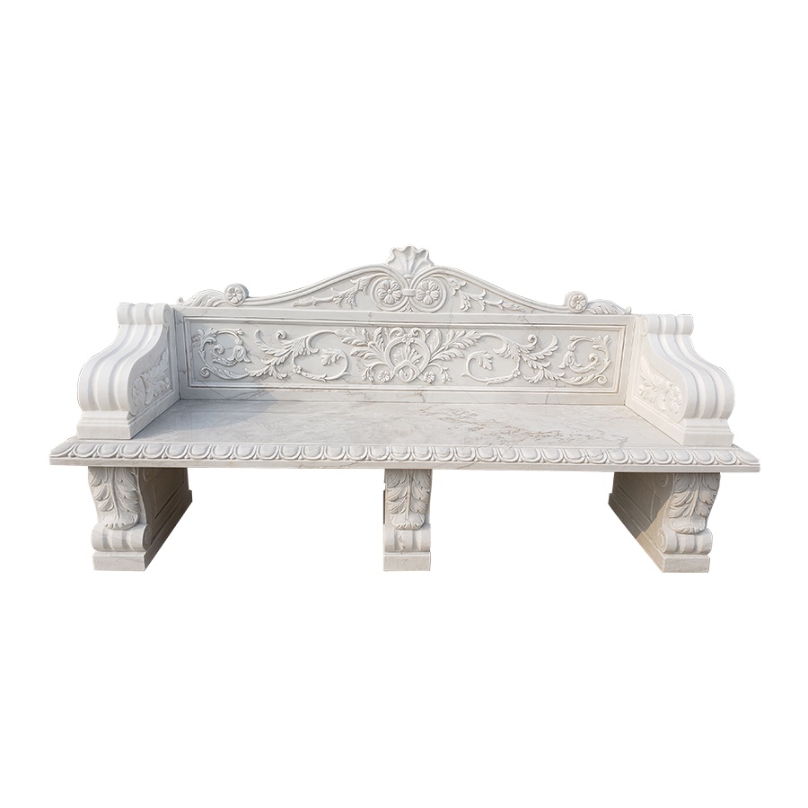 An elegant white marble bench featuring intricate floral and scrollwork carvings on the backrest and armrests, supported by carved legs.