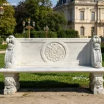 White marble bench featuring ornate carvings and classical detailing against a lush garden backdrop with historic architecture.