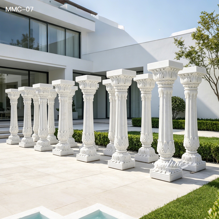 Elegant white marble columns with intricate carvings arranged outdoors near a modern building with landscaped greenery and clean design.