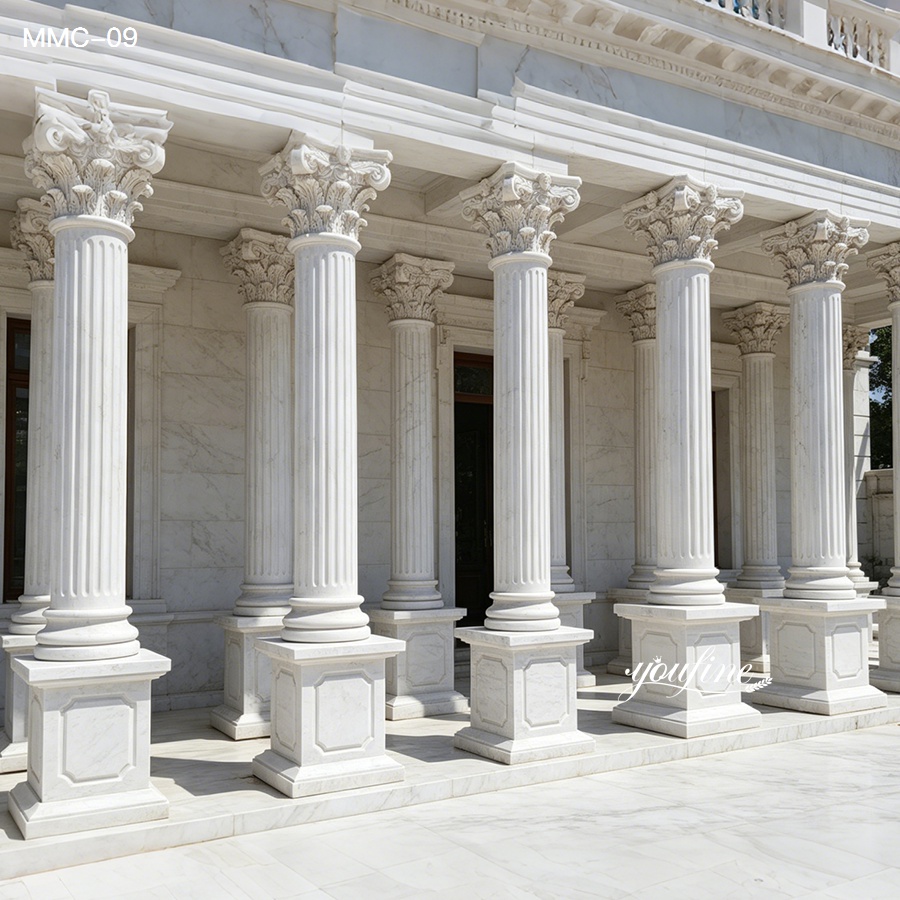 Row of intricately carved white marble Corinthian columns with fluted shafts and ornate capitals in an architectural setting.
