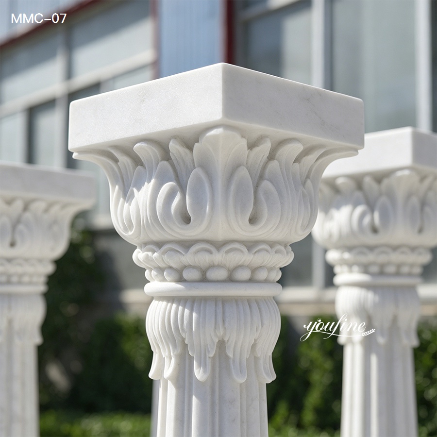 Elegant white marble Corinthian columns featuring intricate floral carvings, displayed outdoors with architectural background.