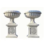 Pair of white marble decorative urns with ornate floral detailing on square pedestals, showcasing elegant craftsmanship.