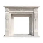 Elegant white marble fireplace mantel featuring intricate carved details, including floral and leaf patterns, on a bright background.