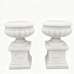 A pair of white marble garden planters with intricate carvings and decorative pedestals, showcasing refined craftsmanship.