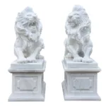 Two detailed white marble lion statues on intricately carved pedestals; one roaring and the other with a calm expression.