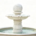 Elegant white marble fountain with tiered bowl design, ornate carving, and water flowing into a basin below.
