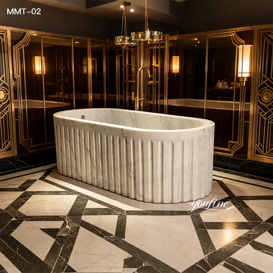 Ornate white marble bathtub with fluted design in a luxurious bathroom featuring patterned marble floors and gold-accented decor.