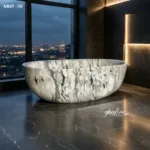 Elegant oval marble bathtub with a unique black and white veined pattern, placed in a modern bathroom overlooking a cityscape at dusk.